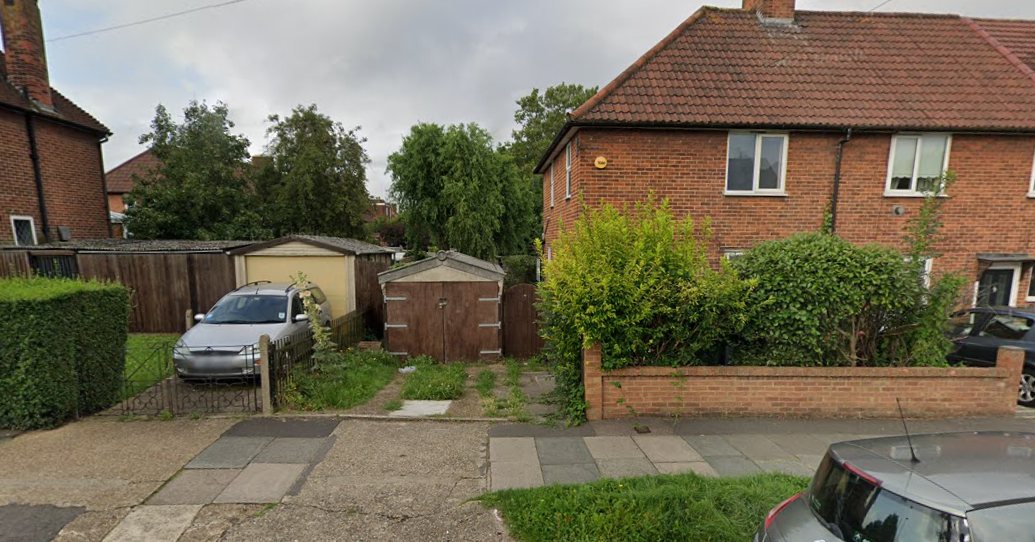 The site as it was: two lock-up garages and a hardstanding to the side of the end house, which still has its original hipped roof sloping away at the corner. That hipped roof is what you would expect a new house next door to have to copy.